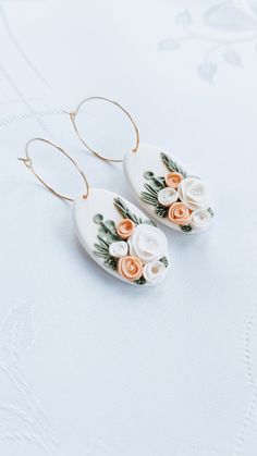 two white and orange flowers are hanging from the back of some gold hoop earrings on a white surface