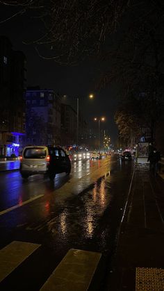 cars driving down the street at night in the rain with lights on and buildings behind them