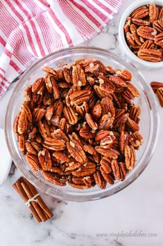 two bowls filled with pecans on top of a marble counter next to cinnamon sticks