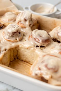 a white dish filled with cinnamon rolls covered in icing and sitting on a table