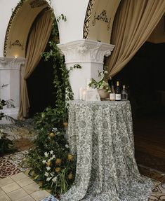 a table covered with flowers and candles in front of two archways that are decorated with greenery