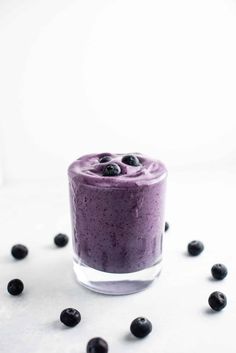 blueberry smoothie in a glass with fresh blueberries around it on a white surface