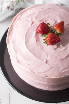 three strawberries on top of a pink frosted cake