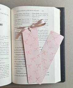 an open book with pink paper tags tied to it's sides and ribbon on top