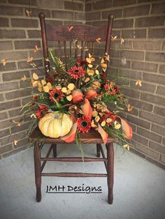 a wooden chair with flowers and pumpkins on the back is sitting in front of a brick wall