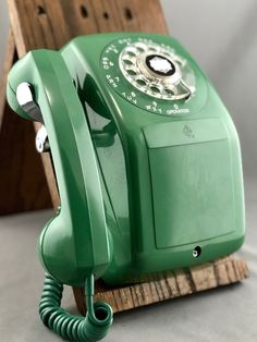 an old green phone sitting on top of a wooden stand