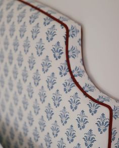 an upholstered headboard with blue and white designs on the fabric, along with red piping