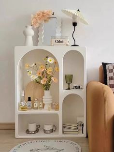 a white shelf with vases, candles and flowers on it in a living room