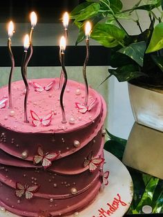 a birthday cake with pink frosting and butterflies on it, surrounded by greenery