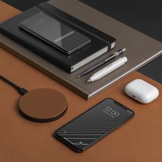 an electronic device, mouse, cell phone and pen on a brown table with notebooks