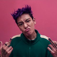 a young man with purple hair and piercings on his fingers, making a face