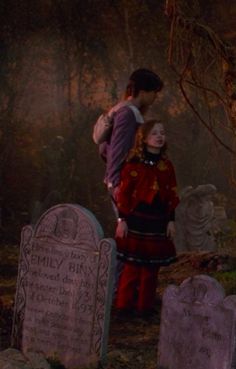 a man and woman standing next to each other in front of tombstones at night