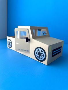 a cardboard box shaped like a car with wheels and tires on the side, sitting on a blue surface