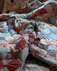 an unmade bed is covered with colorful quilts on the floor next to a window