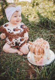 a baby sitting in the grass next to a cake with a hedge on it's side