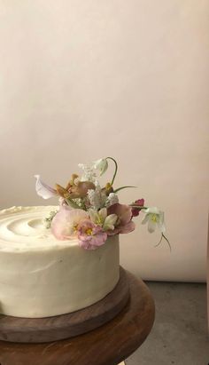 a white cake sitting on top of a wooden table next to a vase with flowers