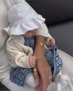 a woman holding a baby wearing a white hat and blue jeans on top of a couch