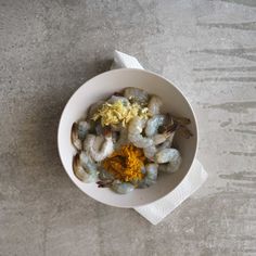 a white bowl filled with food sitting on top of a cement floor next to a napkin