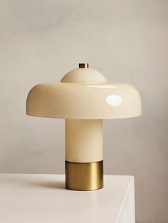 a white and gold table lamp sitting on top of a white countertop next to a gray wall