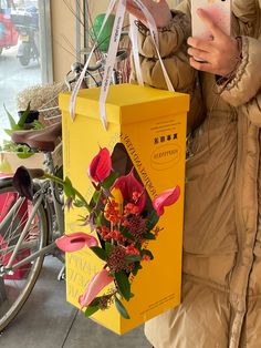 a woman holding a yellow shopping bag with flowers in it