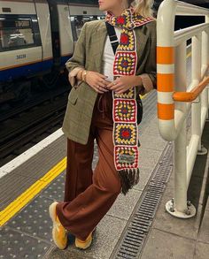 a woman is standing on the platform with her hand in her pocket and wearing a scarf around her neck