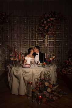 a bride and groom kissing at their wedding table with candles in front of the cake