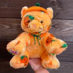 an orange stuffed animal with green and red paint on it's face is held in front of a wooden wall