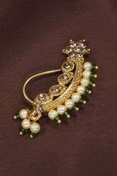 This traditional nose pin is crafted in gold-plating and features Pearl beaded clip-on nose ring with chain, connecting to a hook closure. Style this nose pin with your ethnic attires for festive ready look. No piercing required. Perfect Accessory for every jewelrybox. Product Features: color: Green material: Alloy Dimension: Outerdiameter- Height-3 cm, Width- 1cm Occasion: Festive Product Type: Nose ring Disclaimer: There will be slight difference in digital to actual image Green Nose Ring, Nose Ring With Chain, Ring With Chain, Bridal Nose Ring, Nose Pin, Pearl Stone, Green Material, Pearl Beads, Gold Plating