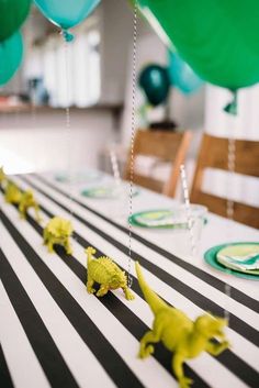 the table is decorated with green and blue balloons, dinosaur figurines, and black and white stripes