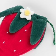 a strawberry shaped bag with a flower on the front and green sleeves, sitting on a white surface