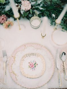 the table is set with plates, silverware and pink flowers on top of it