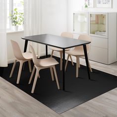 a dining room table with four chairs and a rug on the floor in front of it