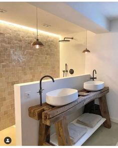 two white sinks in a bathroom with wood accents and brick wall behind them, along with wooden stools