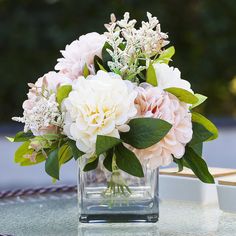 a vase filled with white and pink flowers on top of a glass table covered in greenery