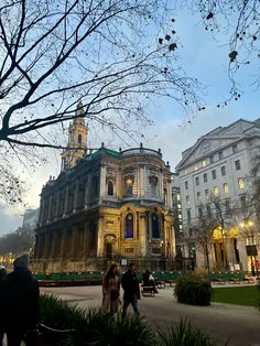 people are walking around in front of some old buildings at dusk, with the lights on