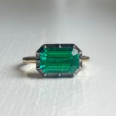 The Georgian-Victorian Emerald Cut Emerald & Blackened Gold East West Button Back Collet Ring—a timeless engagement piece inspired by the grace of the Georgian and Victorian periods. This ring, featuring a stunning 3 ct lab-grown emerald in a Georgian cut-down collet setting and button back, exudes a timeless yet modern charm. It's not just an engagement ring; it's a versatile piece designed for stacking and layering with other styles. Lab Grown Gems: Our lab grown stones are not synthetic, or t Classic White Gold Emerald Ring For Proposal, Classic Emerald Cut Ring With Ethically Sourced Gemstones, Classic Octagon Emerald Ring In Platinum, Timeless Emerald Ring With Prong Setting, Timeless Emerald Gemstone Wedding Ring, Classic Emerald Ring For Proposal, Heirloom White Gold Solitaire Emerald Ring, Classic Emerald Ring With Center Stone For Proposal, Heirloom Solitaire Emerald Ring In White Gold