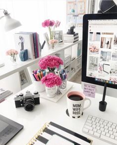 a desk with a computer, camera and pink flowers