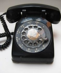 an old black rotary telephone sitting on top of a table