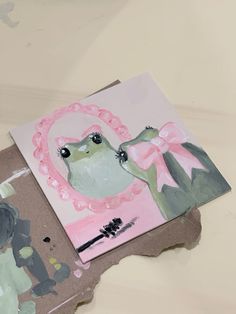 a piece of art that looks like a frog with a pink bow on its head