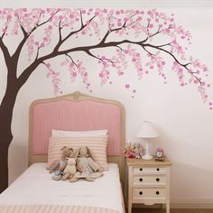 a bedroom with a pink tree painted on the wall and stuffed animals under the bed