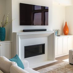 a flat screen tv mounted on the wall above a fireplace in a living room with white furniture