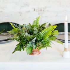 there is a plant in the center of the table with a candle on it and plates behind it