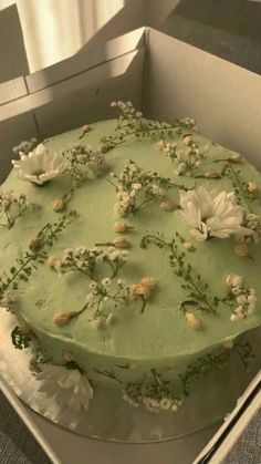 a green cake with white flowers on top in a box, ready to be eaten