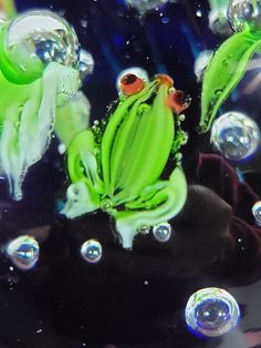 a green frog sitting on top of a black object with bubbles around it's legs