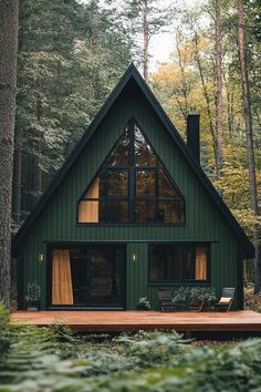 a green cabin in the woods surrounded by trees and foliage, with a deck leading up to it