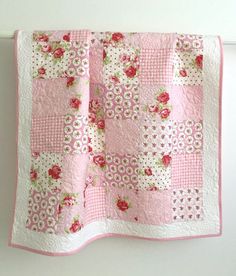 a pink and white quilt with roses on it, hanging from a hook in a wall