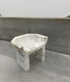 a white marble bench sitting on top of a cement floor next to a concrete wall