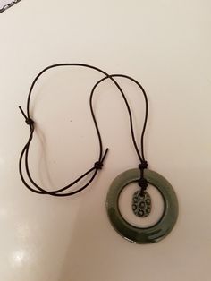 a green necklace with a circular pendant hanging from it's side on a white surface