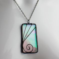 "Transparent wavy, iridescent pale pink stained glass pendant edged in silver, accented with silver wire and treated with a black patina finish. The iridized glass reflects colors of pink, green, yellow, blue and purple depending on the angle. Add a 17-19\" adjustable black waxed cotton necklace cord for free or purchase an 18\" sterling silver cable chain necklace under options.   Actual Size: 2 1/4\" x 1 1/16\" Each item by Faerie Glass Is 100% uniquely hand-crafted with quality materials that are lead-free. NOTE - All photographs are taken in effort to best represent the actual product. Color of actual jewelry may vary slightly from photographs." Stained Glass Jewelry Pendant, Pink Stained Glass, Soft Solder, Stained Glass Necklace, Stained Glass Pendant, Elven Jewelry, Cotton Necklace, Stained Glass Jewelry, Pink Green Yellow