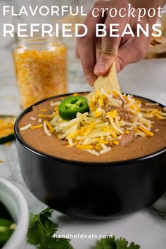 a hand dipping a tortilla chip into a bowl filled with refried beans